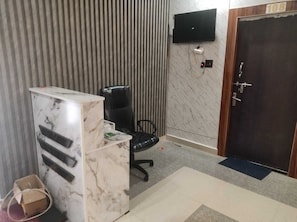 Ein Zimmer mit einem Marmortisch, einem schwarzen Bürostuhl, einem an der Wand befestigten Fernseher und einer Tür mit einer Nummer.'