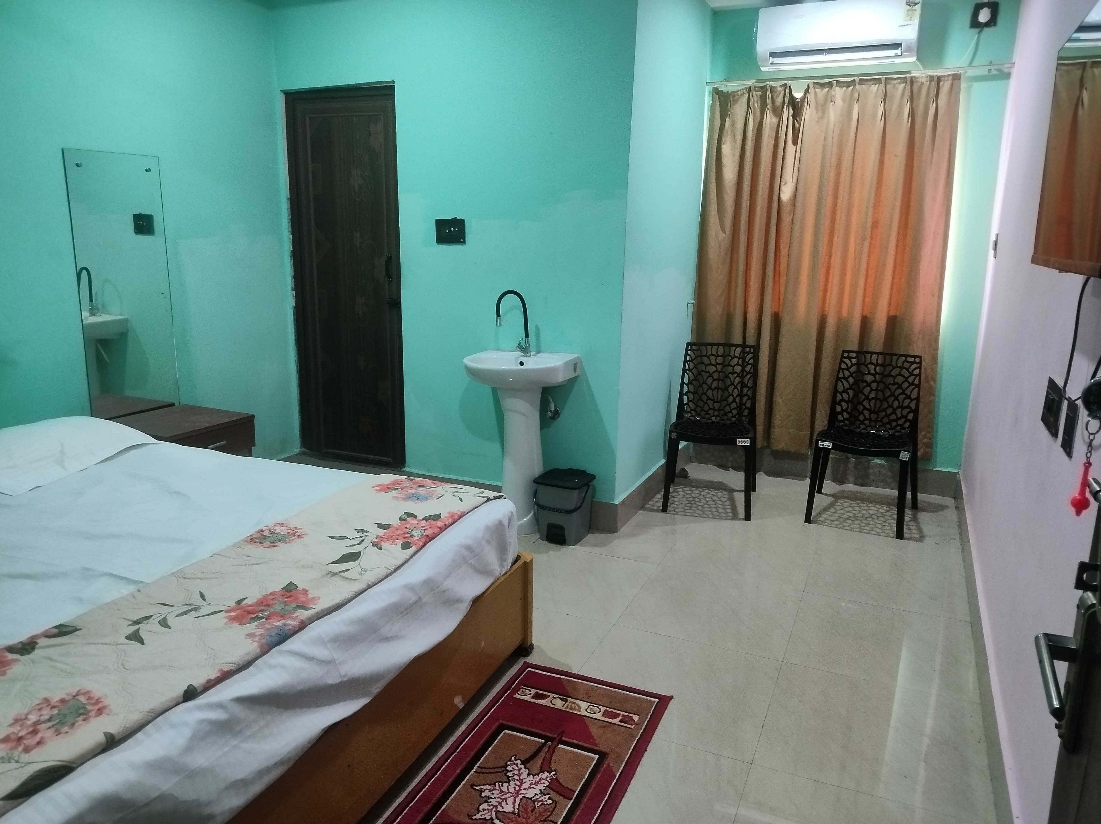 Un dormitorio con cama, lavamanos, dos sillas y ventana con cortinas.