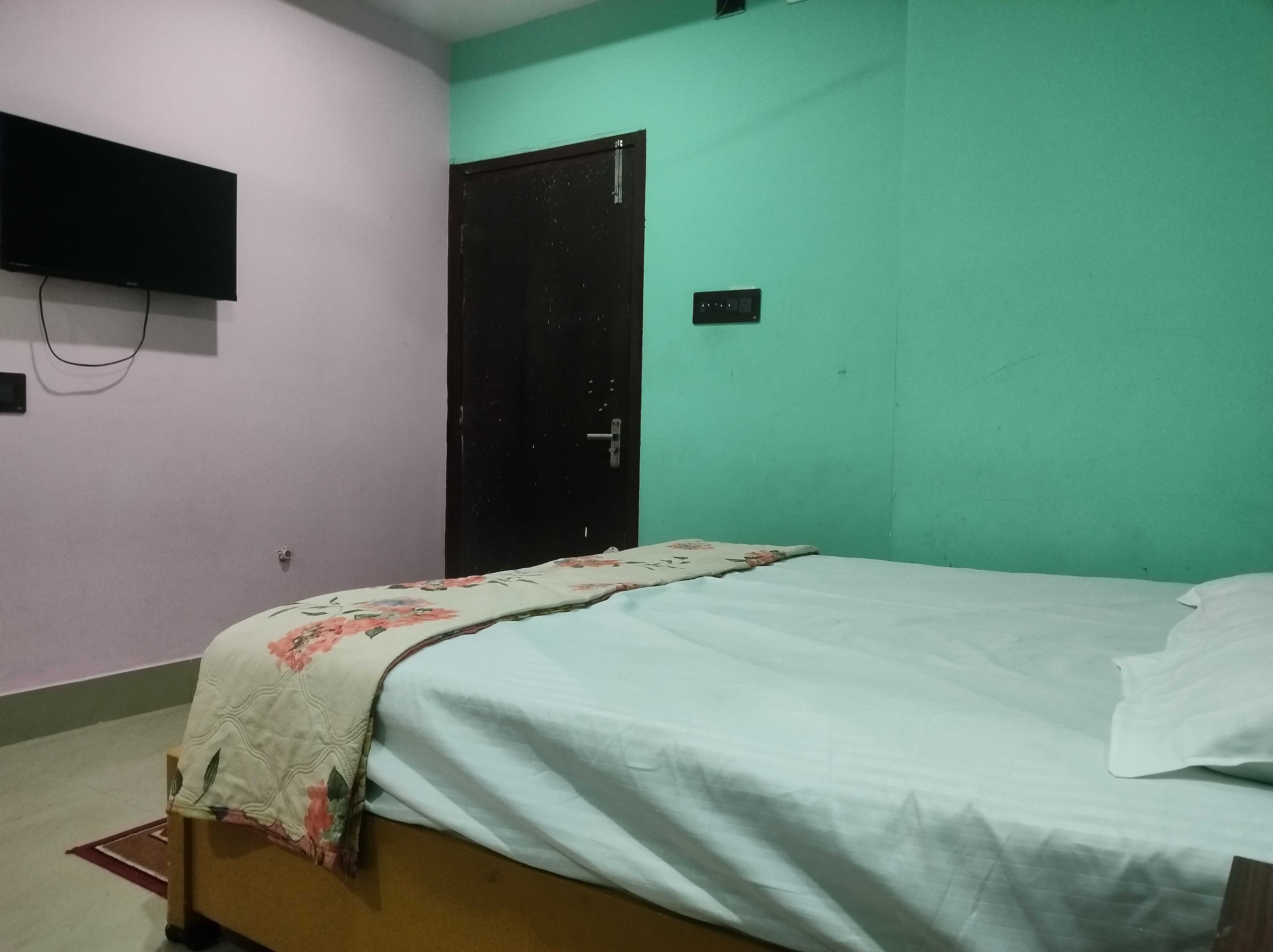 Una habitación con una cama, un televisor en la pared y una puerta.