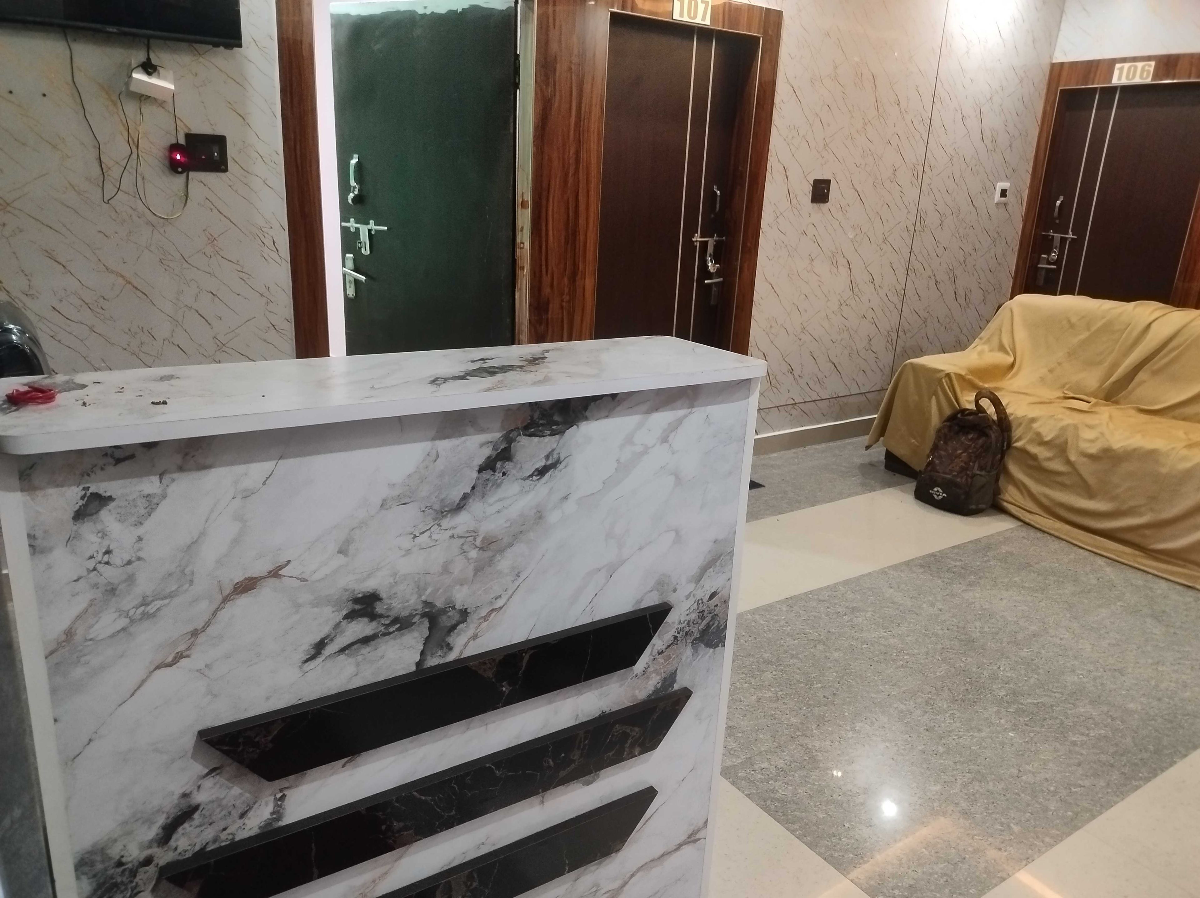 Un mostrador de recepción con acabado de mármol, un perchero con un bolso y una puerta con un cartel de número.
