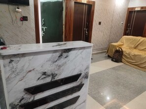 A reception desk with a marble finish, a coat rack with a bag, and a door with a number sign. - Hotel O I Feel Guest House (Khordha)