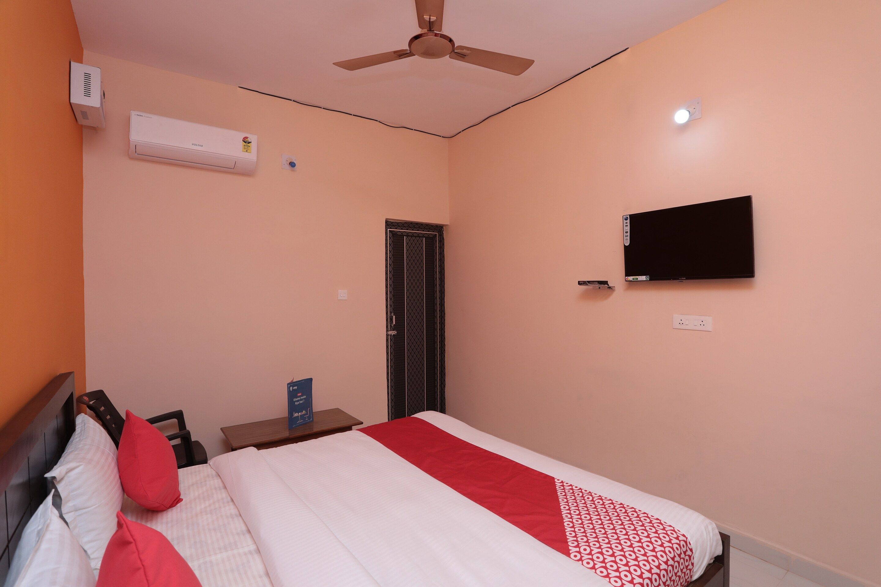 A bedroom with a bed, a ceiling fan, a TV mounted on the wall, and a window with a closed shutter.