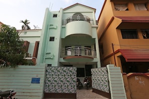 Un edificio residencial de varios pisos con entrada protegida por un portón, un balcón en el segundo piso y una antena parabólica en el techo.