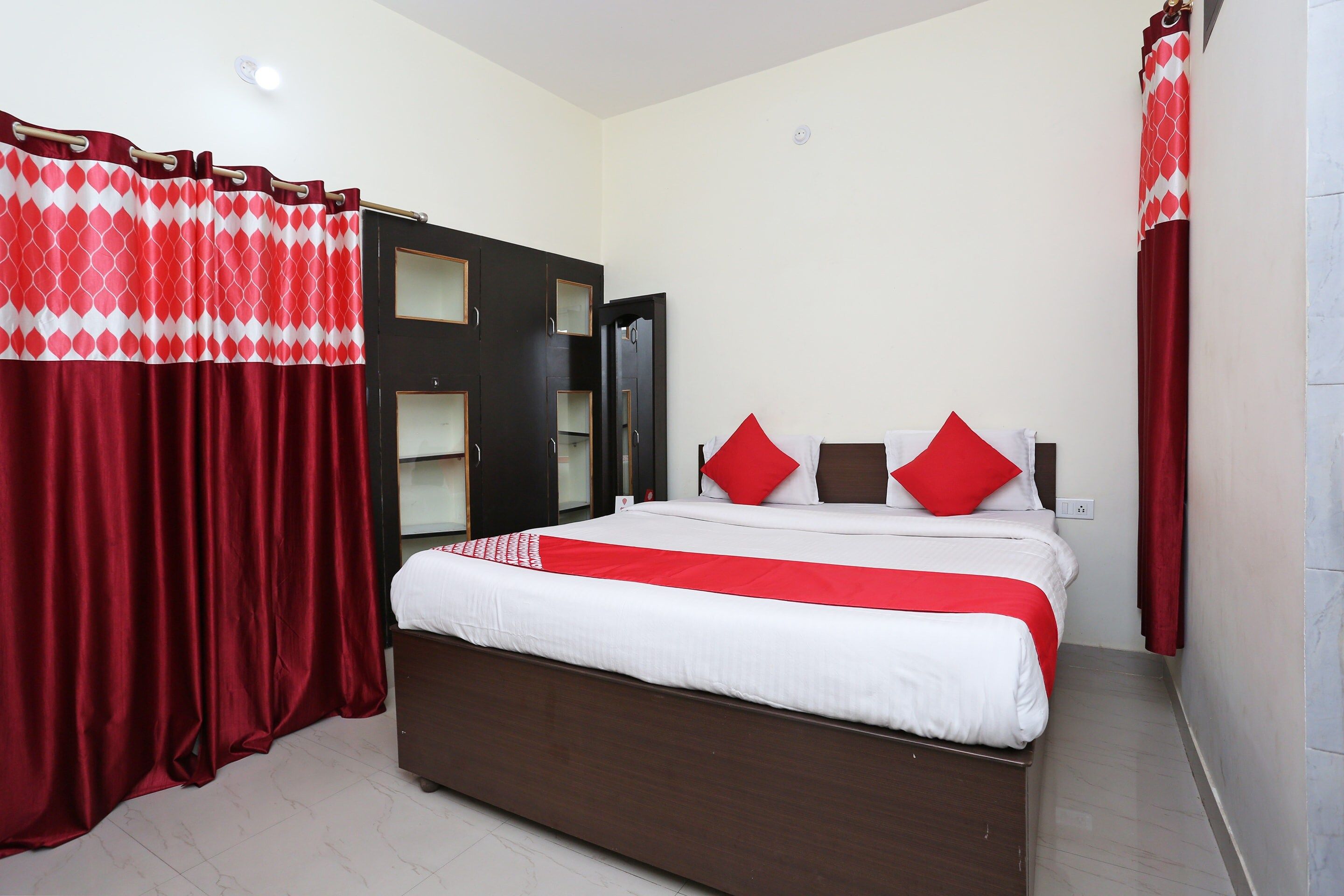 A hotel room with a bed, a wardrobe, and red curtains.