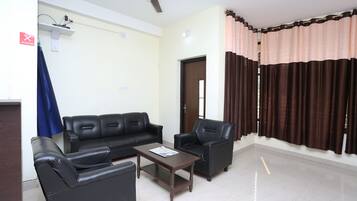 Una sala de estar con sofá, sillones, una mesa de centro, un ventilador de techo y una puerta.