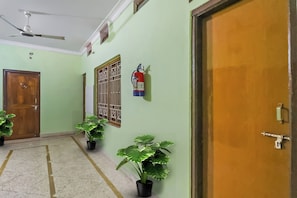 Un pasillo con ventilador de techo, puerta de madera, ventana con barrotes y plantas en macetas.