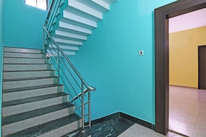 A staircase with metal railings leading to a landing, adjacent to a wall with a light switch. - Hotel O Samrudhi Residency (Bhubaneshwar)