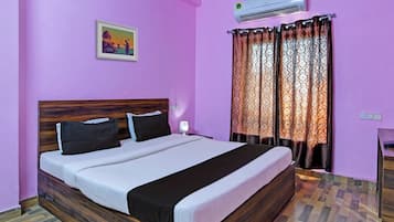 Una habitación con cama, aire acondicionado, un cuadro y cortinas estampadas.