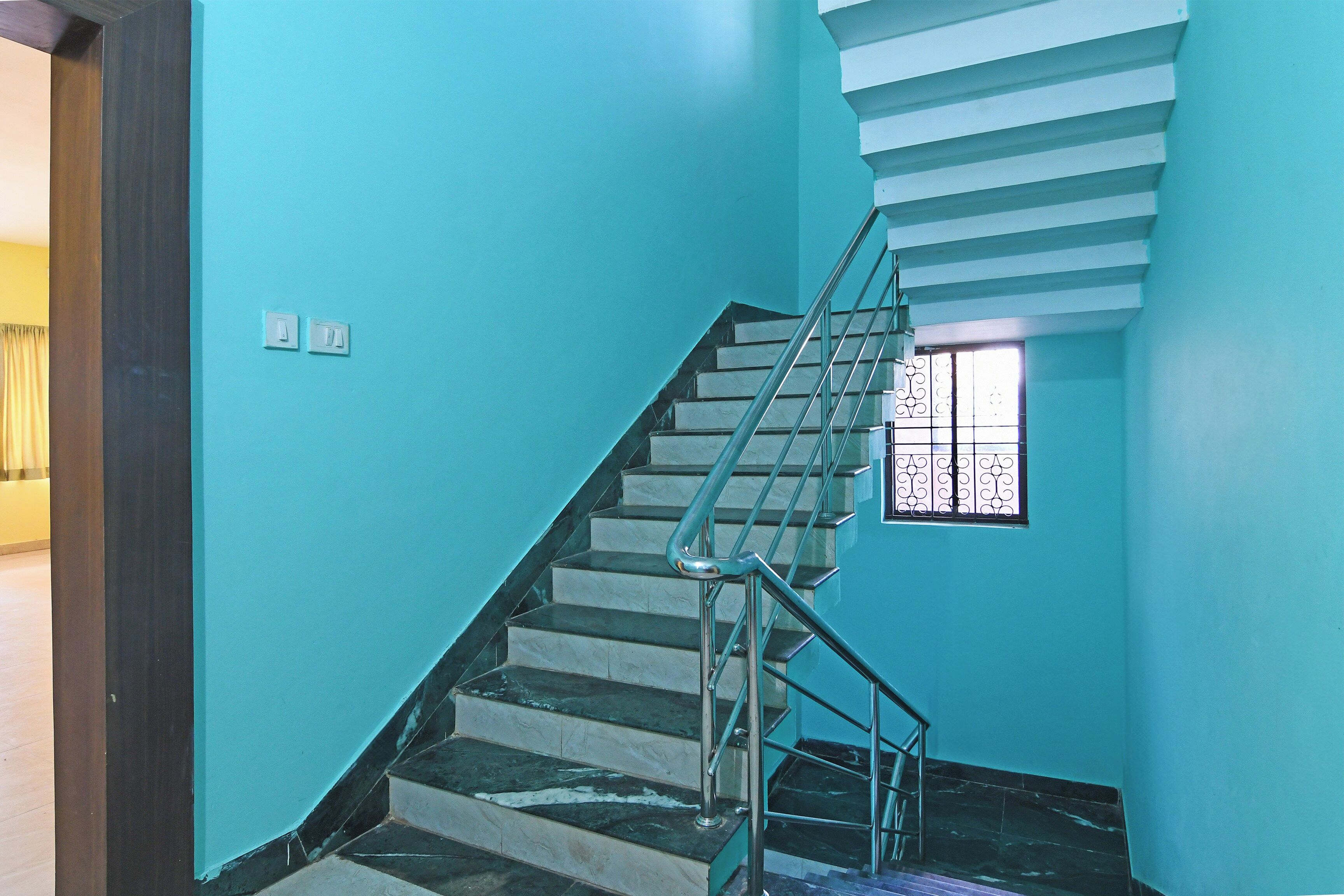 A staircase with a metal railing, a window with decorative bars, and a light switch on the wall.