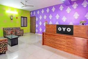 A reception area with a wooden desk, a sofa, and patterned cushions. - Hotel O Samrudhi Residency (Bhubaneshwar)