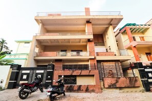Un edificio de varios pisos con balcones, una entrada protegida por una reja y un cartel con el nombre y la dirección.