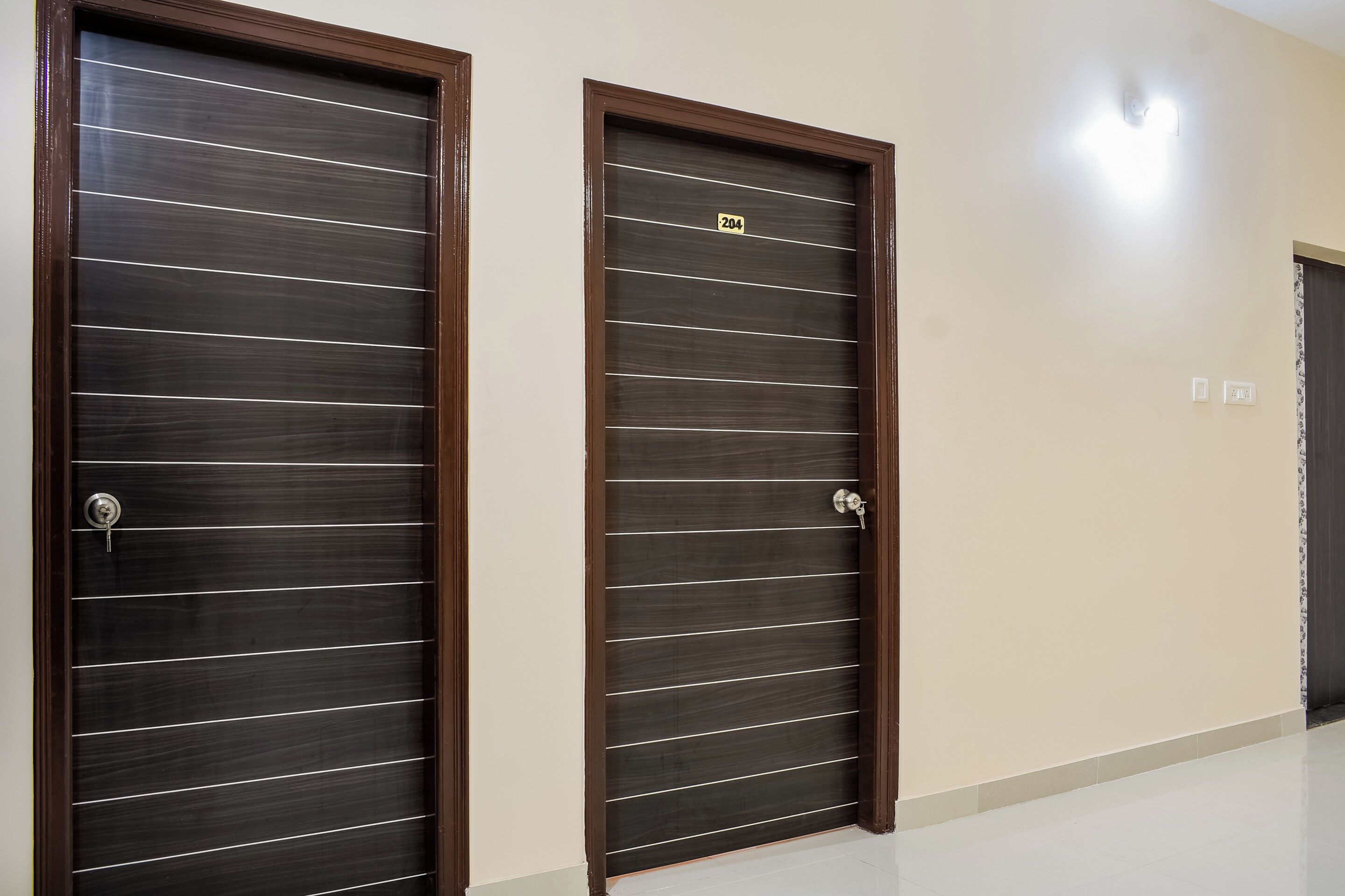 Dos puertas de madera oscura con líneas horizontales y una cerradura, ubicadas en un pasillo con piso y paredes de color claro.