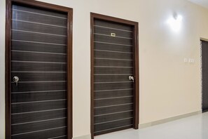 Dos puertas de madera oscura con líneas horizontales y una cerradura, ubicadas en un pasillo con piso y paredes de color claro.