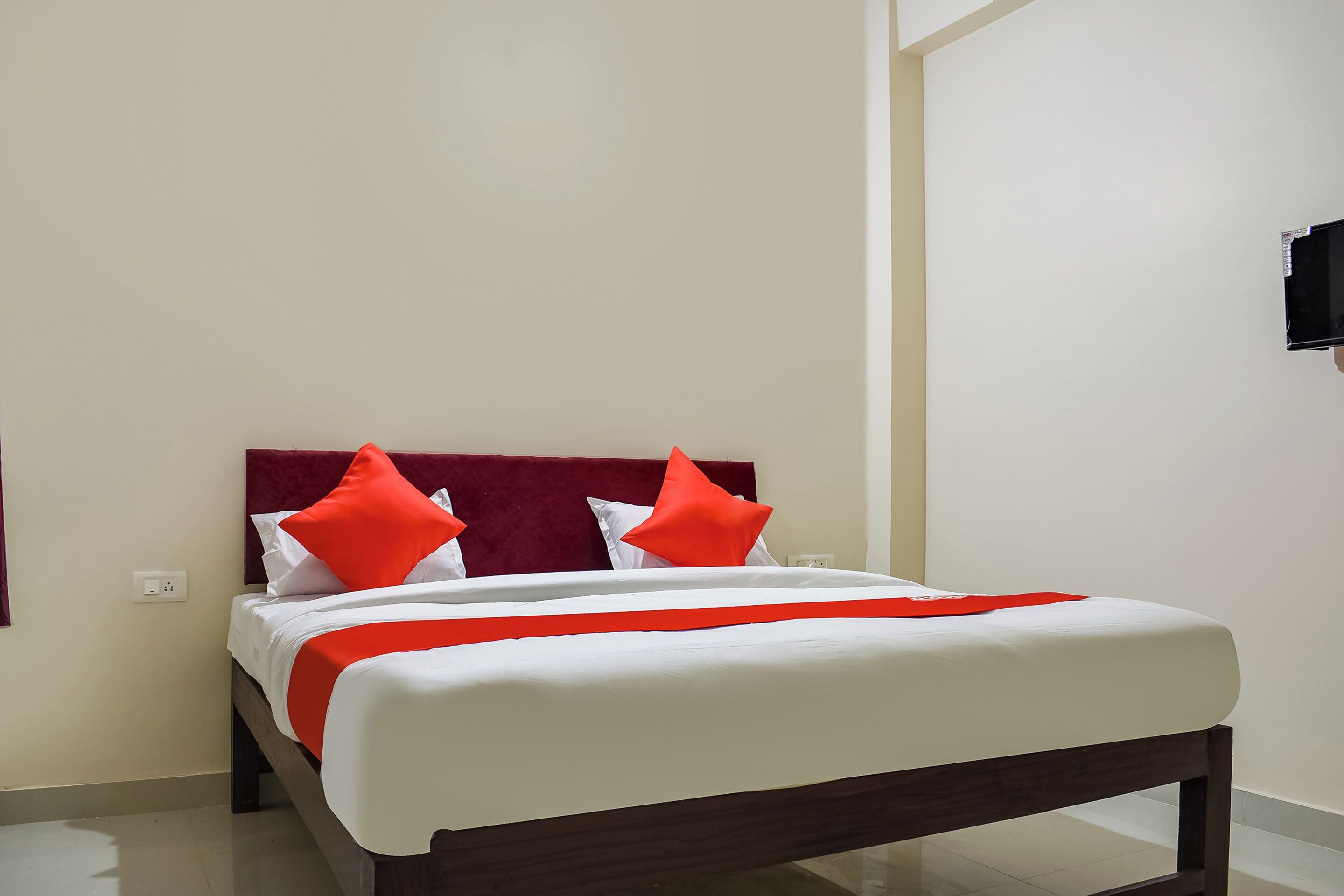Una cama con estructura de madera, ropa de cama blanca y detalles en rojo.