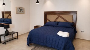 Ein ordentlich bezogenes Bett mit blauer Bettdecke und Kissen, ein kleiner Nachttisch mit Lampe, eine Weltkarte an der Wand und ein hölzernes Kopfteil.