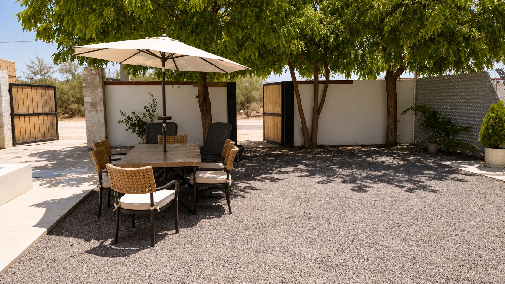 An outdoor patio with a table and chairs, a pergola with an umbrella, and a gravel ground.