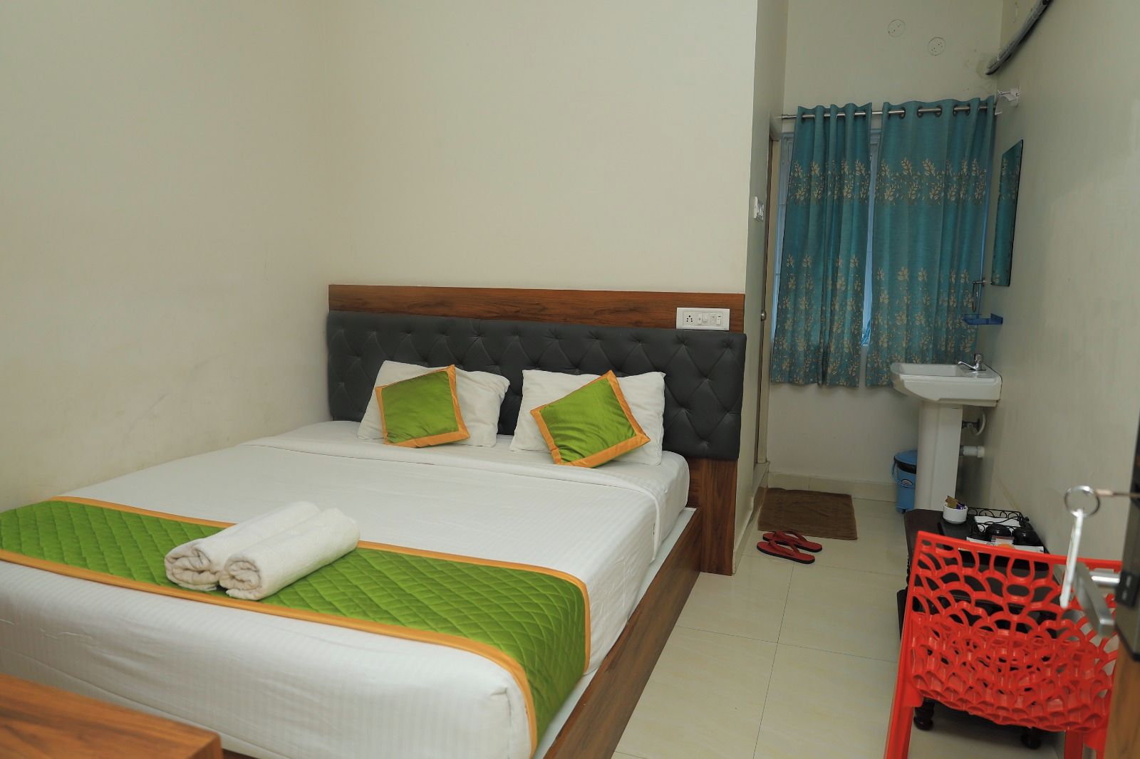 Una cama bien hecha con colcha verde, ropa de cama blanca y dos almohadas con detalles en verde y naranja.