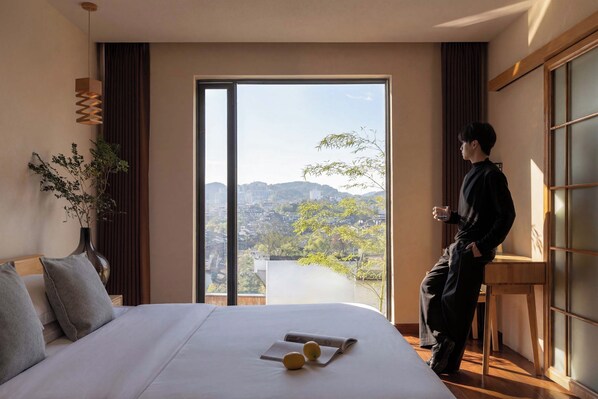 Una habitación de hotel con una cama grande, vistas a la ciudad y una persona de pie junto a la ventana.