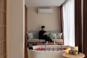 Una persona sentada en un sofá en una habitación con una bañera llena de pétalos de rosa y velas.