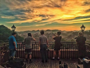 Un grupo de personas en una terraza de madera con vistas a un paisaje urbano al atardecer.