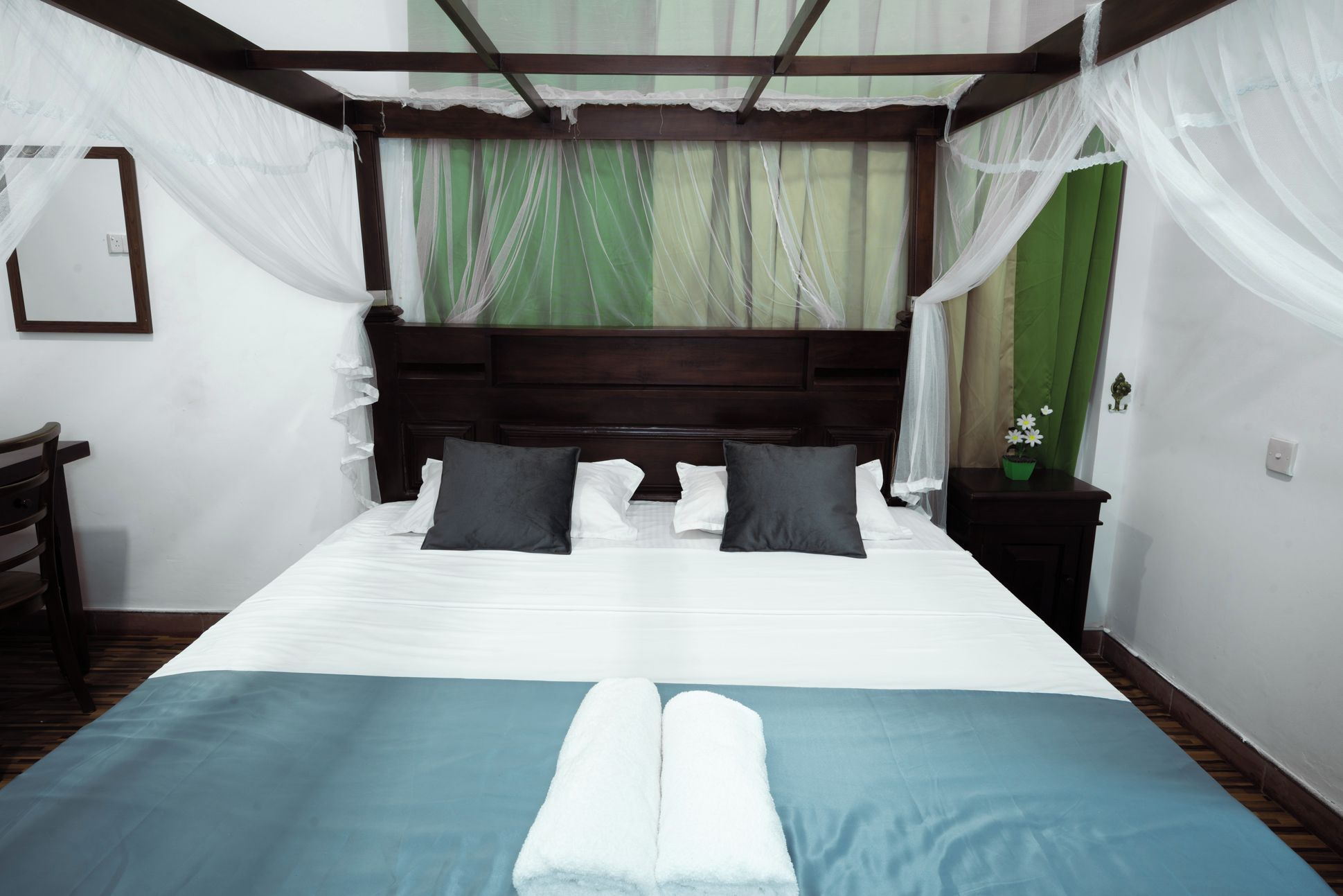 Una cama con dosel, almohadas, una mesita de noche con una planta y una silla.