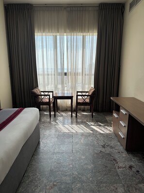 Une chambre d’hôtel avec un lit, un bureau, deux chaises et une vue à travers des rideaux transparents.