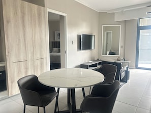 Habitació d'hotel moderna amb taula rodona, quatre cadires, televisió de pantalla plana, mirall i armari.