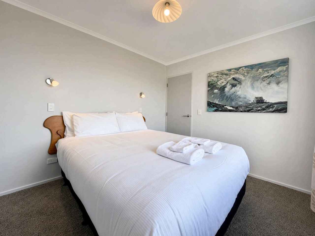 Une chambre d’hôtel avec un grand lit, un tableau au mur et une porte donnant sur une autre pièce.