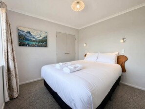 Une chambre d’hôtel avec un lit, un tableau au mur, une porte et un luminaire.