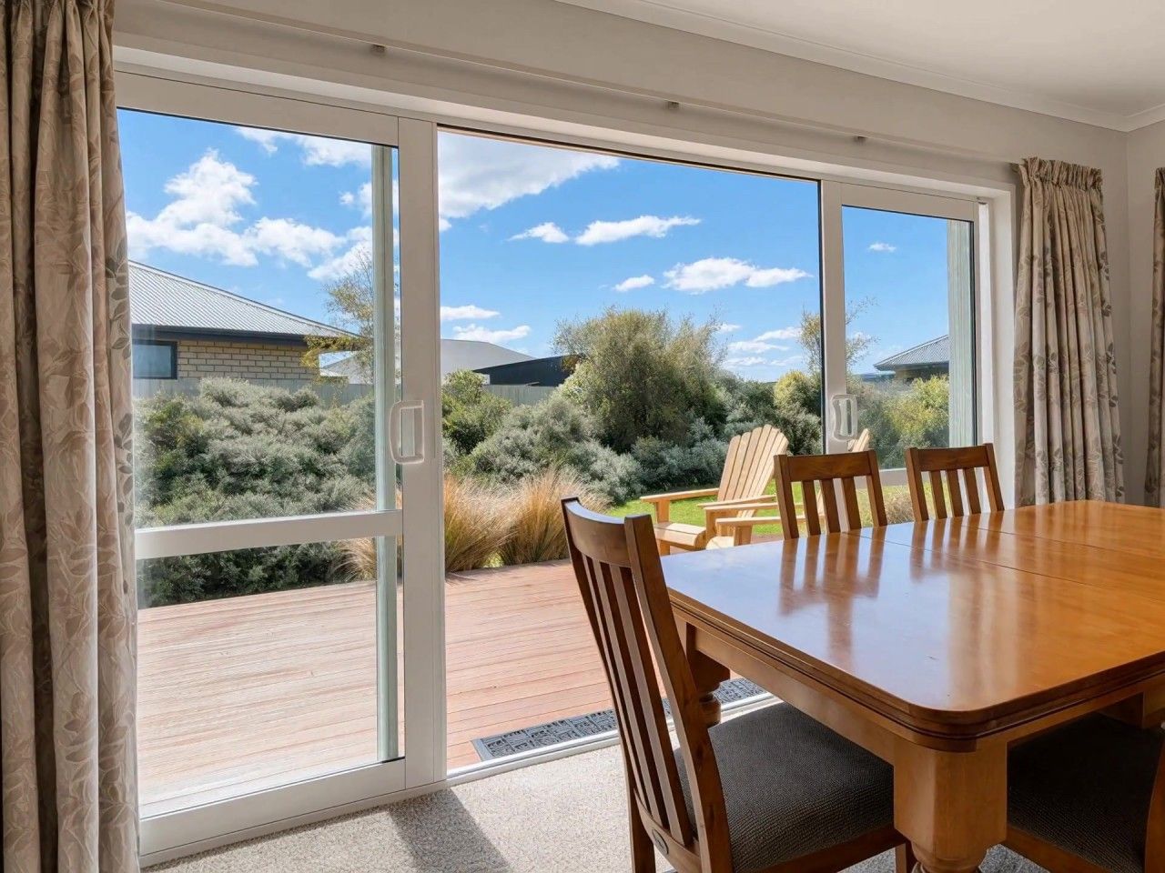 Un espace repas comprenant une table et des chaises, de grandes portes-fenêtres coulissantes donnant sur une terrasse extérieure, et une vue sur le paysage environnant.