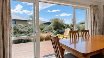 Un espace repas comprenant une table et des chaises, de grandes portes-fenêtres coulissantes donnant sur une terrasse extérieure, et une vue sur le paysage environnant.