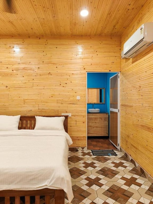 A wooden-paneled room with a bed, a bathroom with a blue sink, and a patterned floor. - The Racha Agonda (Agonda)