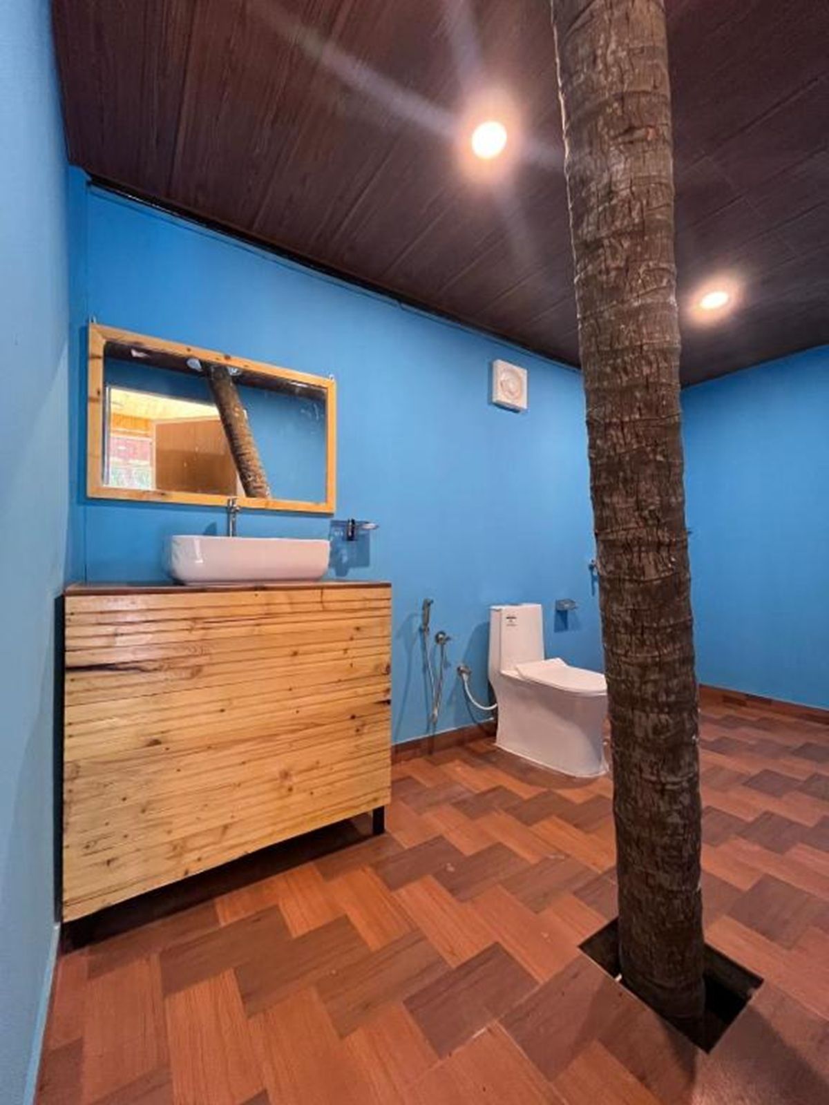 A bathroom with a wooden vanity, a white sink, a mirror, a bathtub, and a tree trunk.