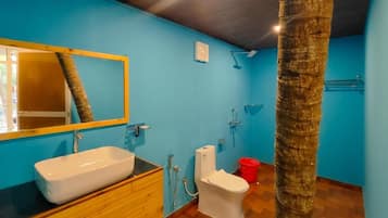 Un baño con tocador de madera, lavamanos blanco, inodoro y zona de ducha.