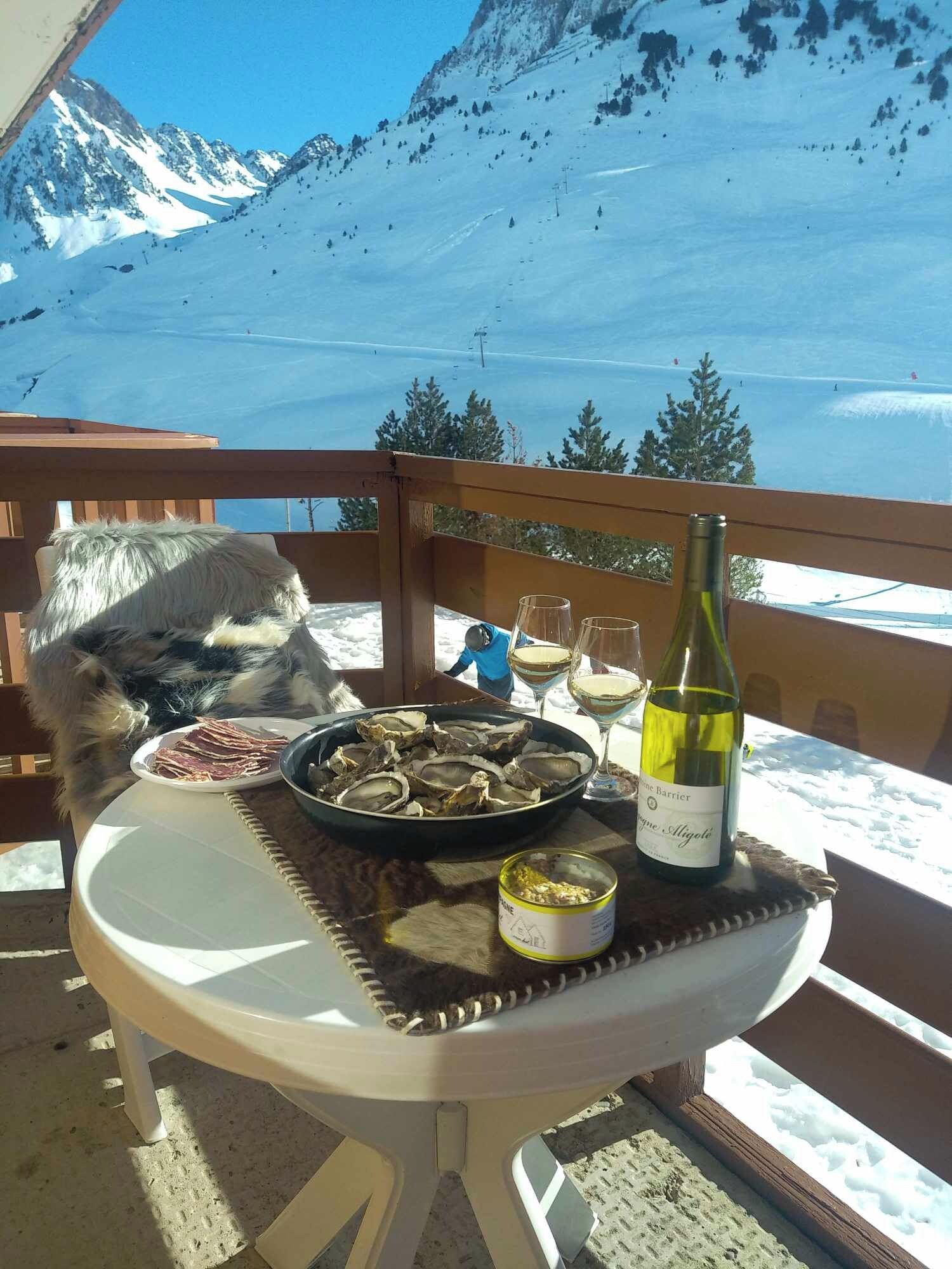 A table with food and drink, a bottle of wine, and a view of snow-covered mountains.