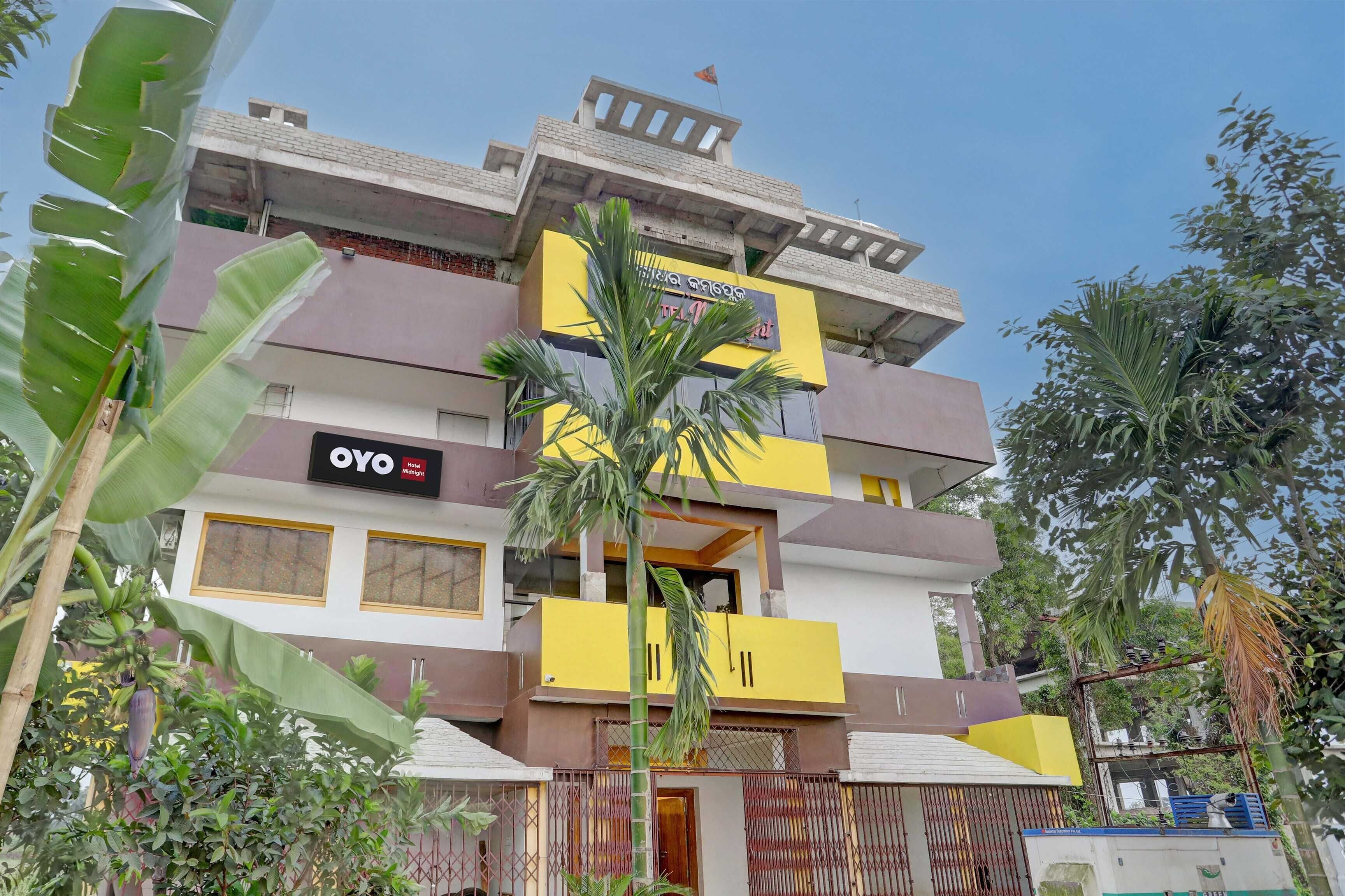 Un hotel de varios pisos con balcones, un cartel que dice 'OYO Hotel Midnight' y follaje circundante.