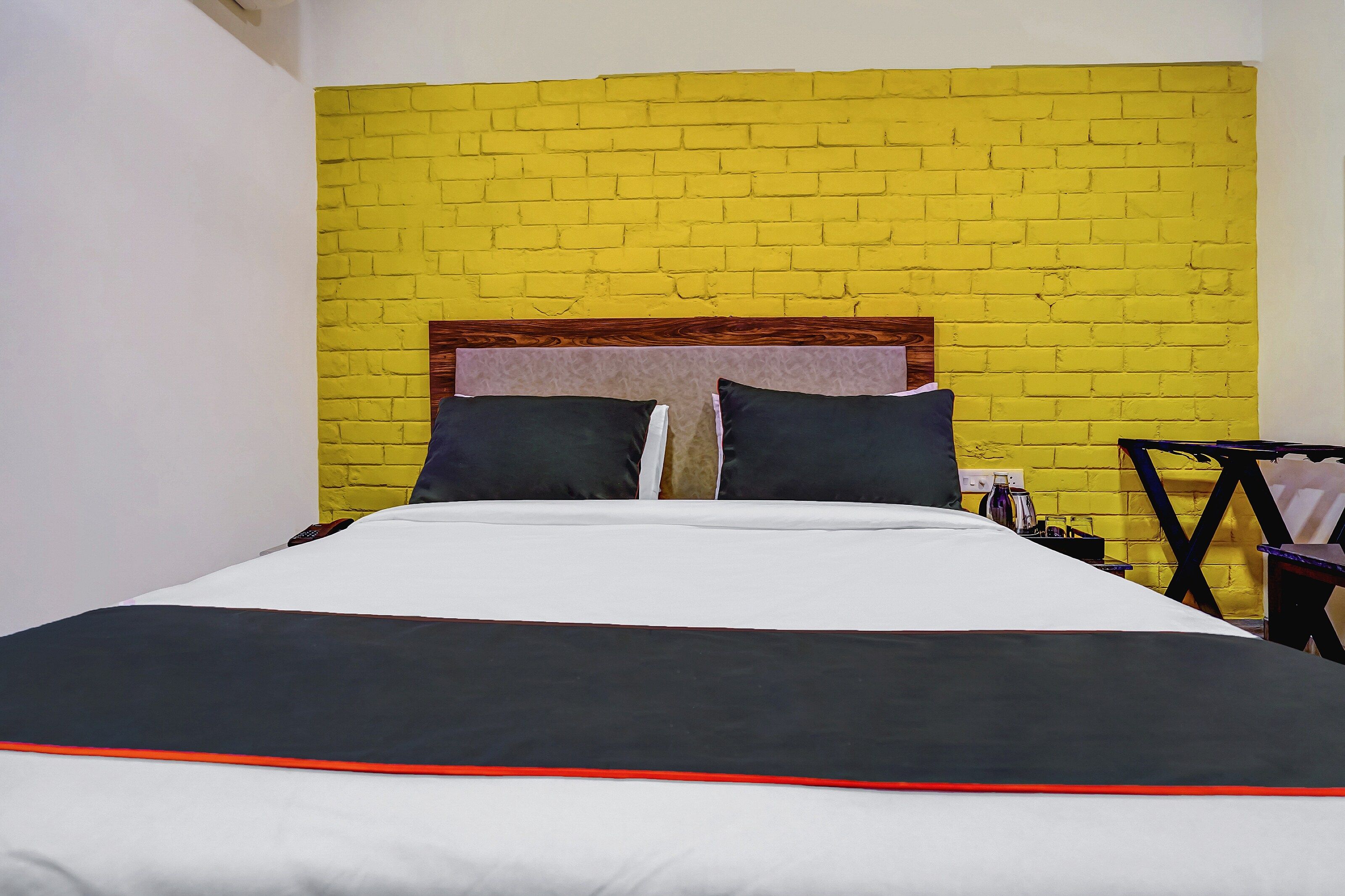 A hotel room with a bed, a nightstand, and a yellow brick wall.