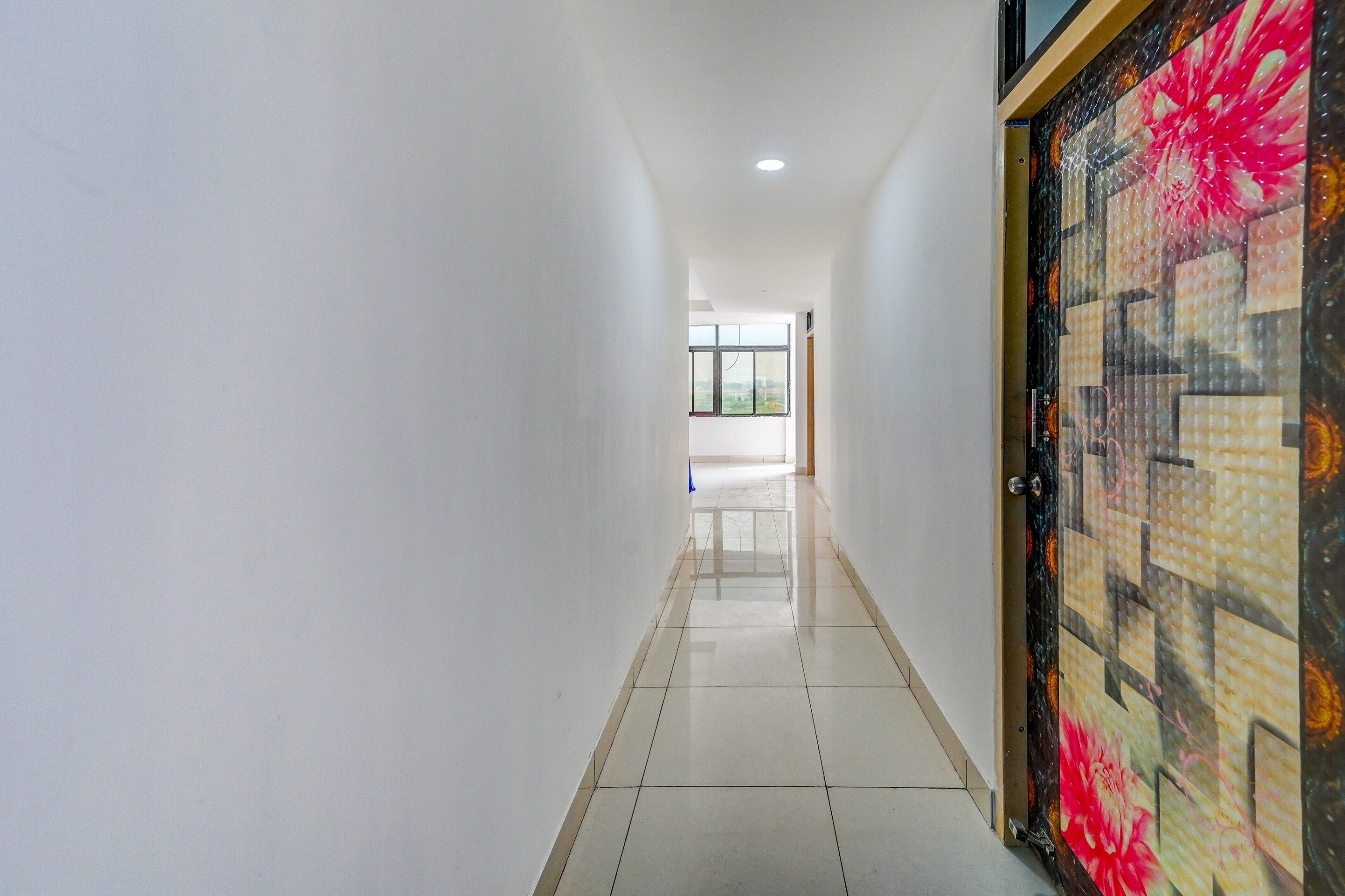A hallway with white walls, a tiled floor, and a door with a floral pattern.