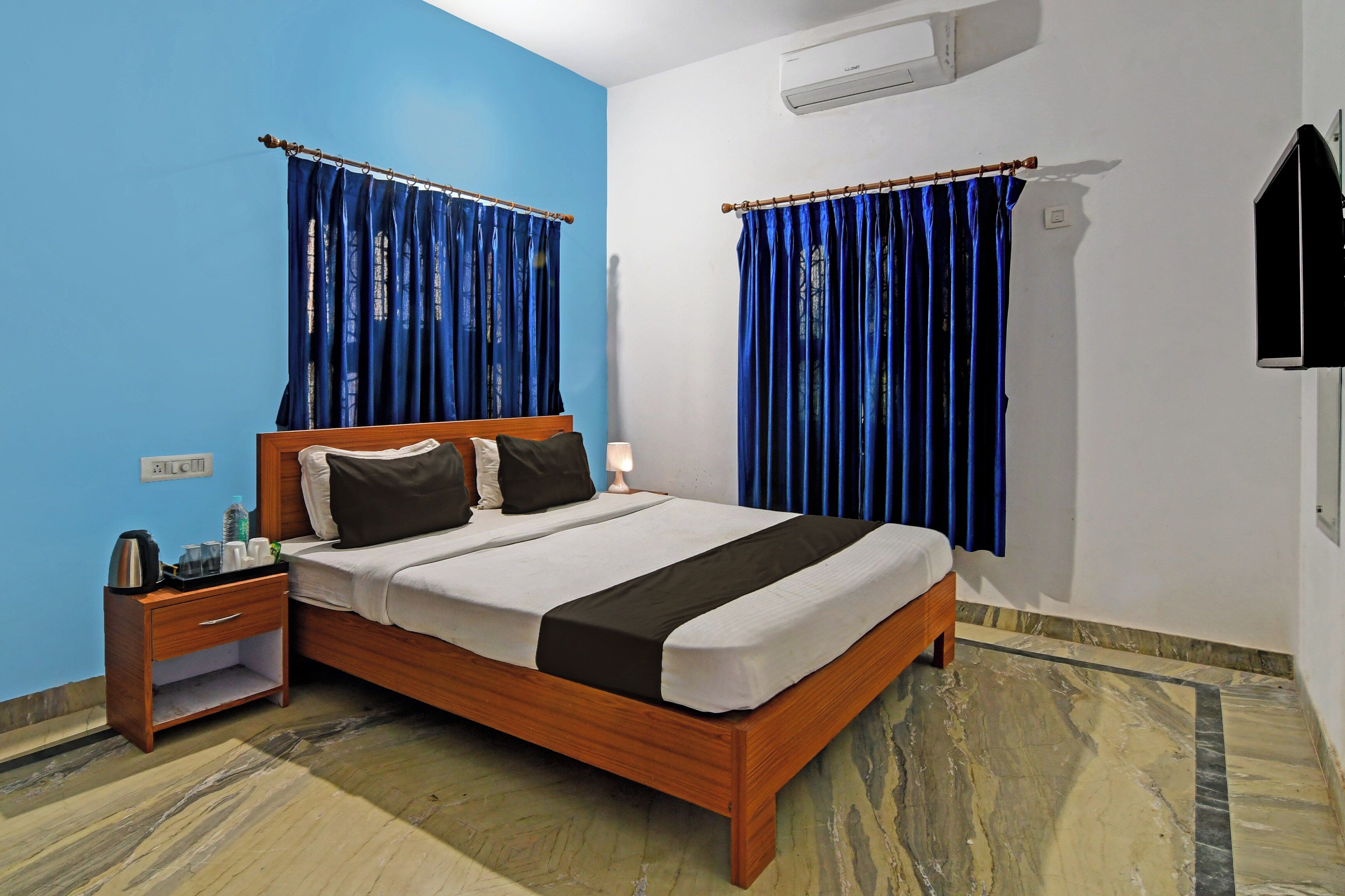 A hotel room with a wooden bed, a nightstand with a lamp, and a blue wall.