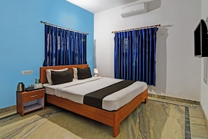 A hotel room with a wooden bed, a nightstand with a lamp, and a blue wall. - Hotel O Home Elite Stay Near Shri Shri (Bhubaneswar)