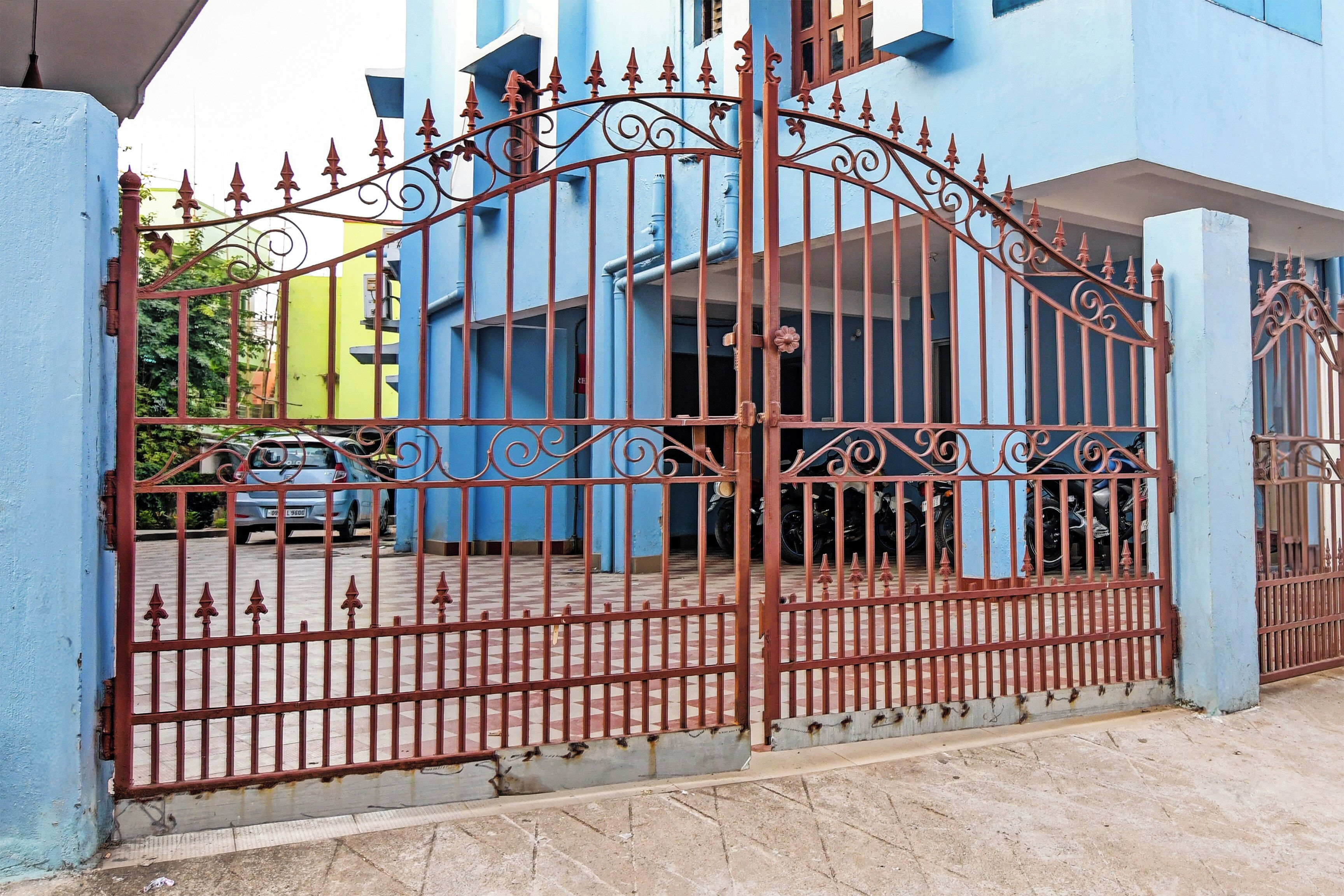 A gated entrance with a metal gate, a paved driveway, and a building with blue walls.