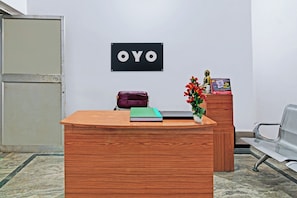 Ein Empfangsschalter mit einem Schild, auf dem 'OYO' steht. Auf dem Schalter liegt eine violette Tasche, ein grünes Buch und eine kleine Statue.