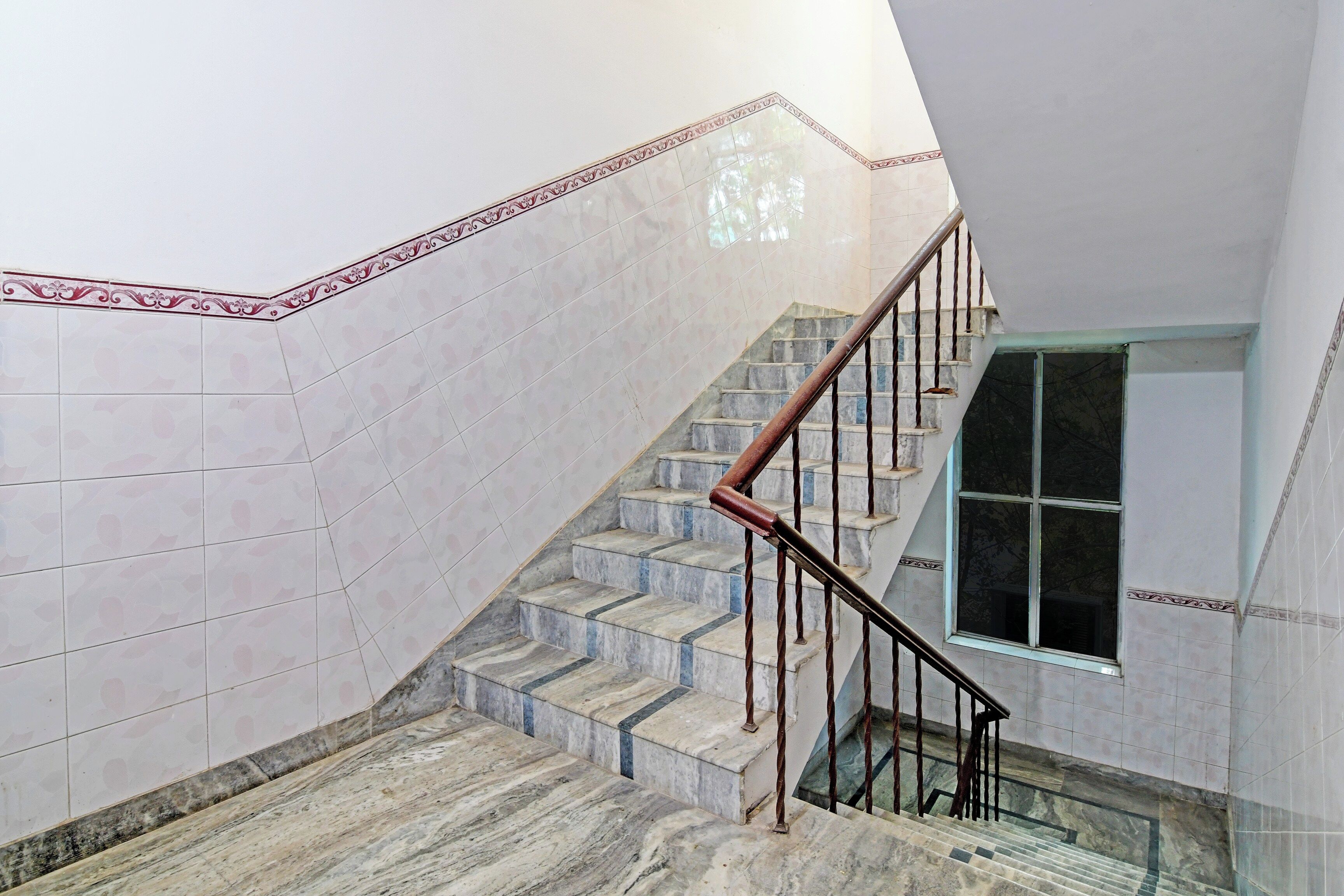 Eine Treppe mit Marmorstufen und einem Metallgeländer, die zu einer Zwischenebene mit einem Fenster führt.