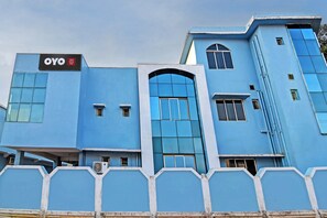 Ein Hotelgebäude mit blauer Fassade, einer Beschilderung mit der Aufschrift 'OYO Hotel Ashrey Stays' und einem großen Bogenportal.