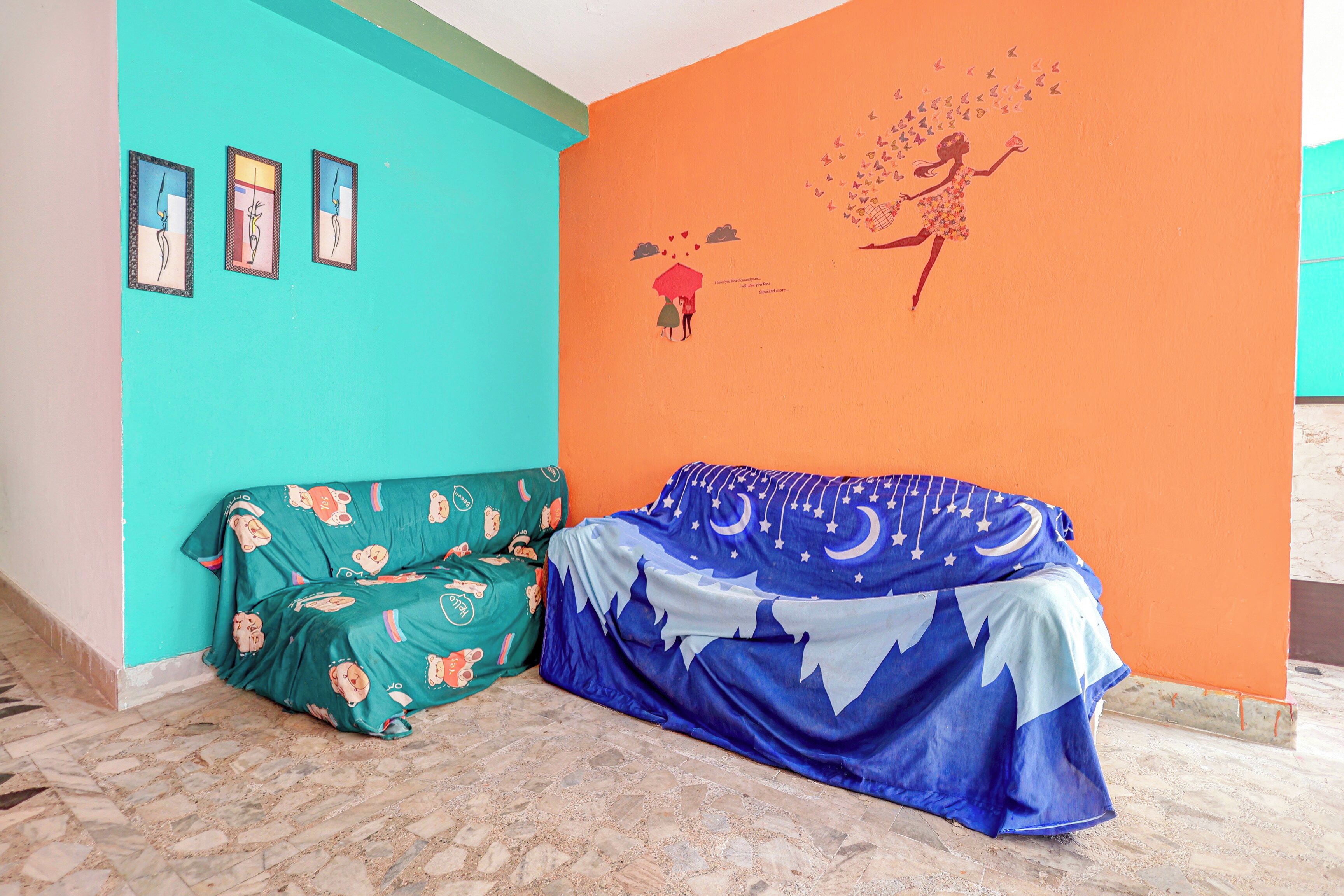 A room with a teal wall, a mural of a woman with butterflies, a green sofa with bear prints, and a blue blanket with a starry pattern.