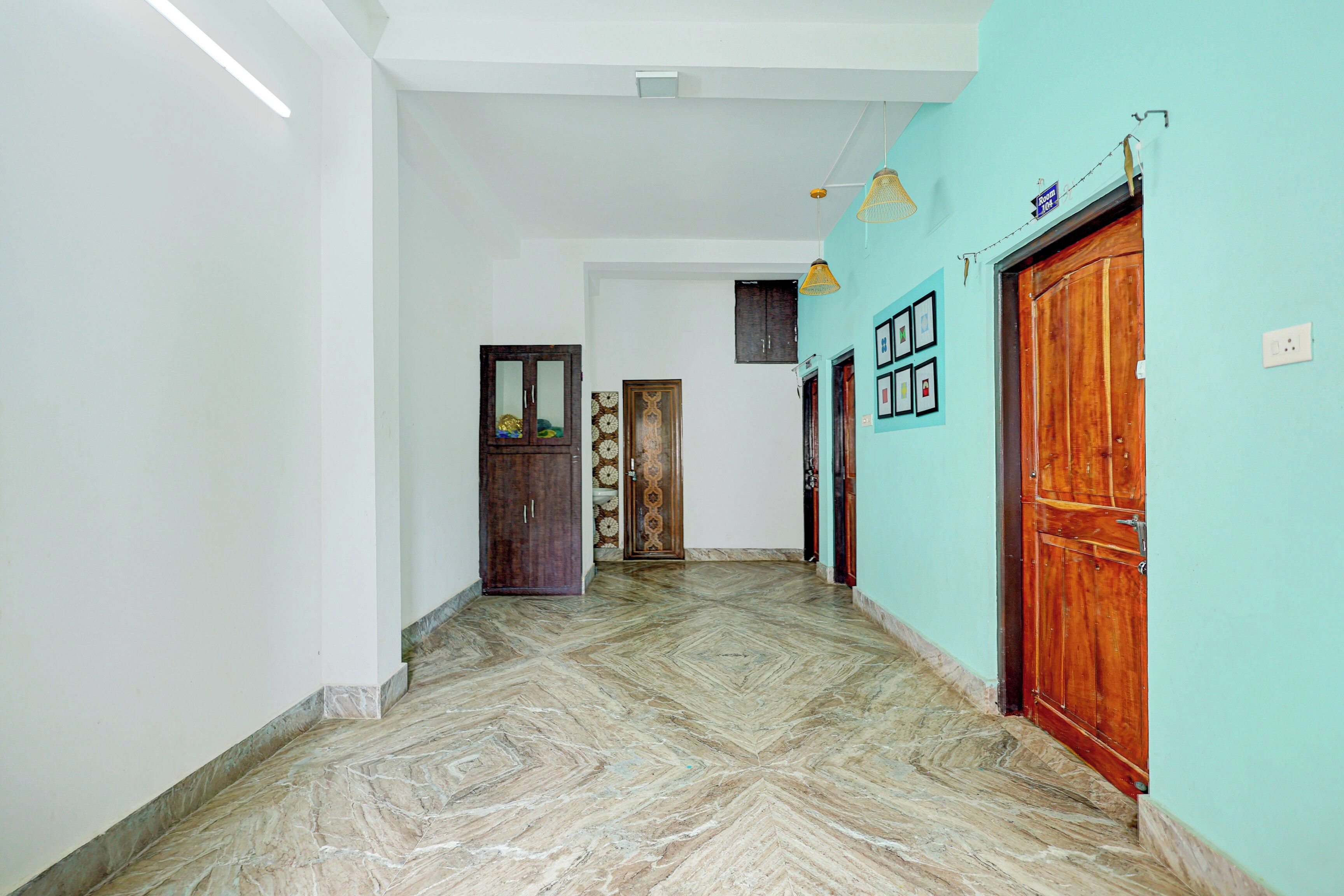 A hallway with a marble floor, a wooden door, and a wall with framed pictures.