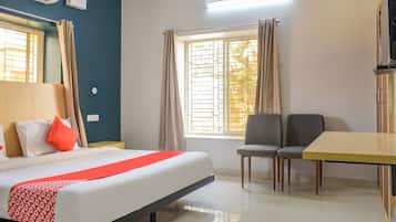 Habitación de hotel con cama, escritorio, dos sillas, ventana con cortinas y unidad de aire acondicionado.