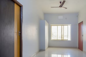 Quarto com ventoinha no teto, janela com persianas e porta.