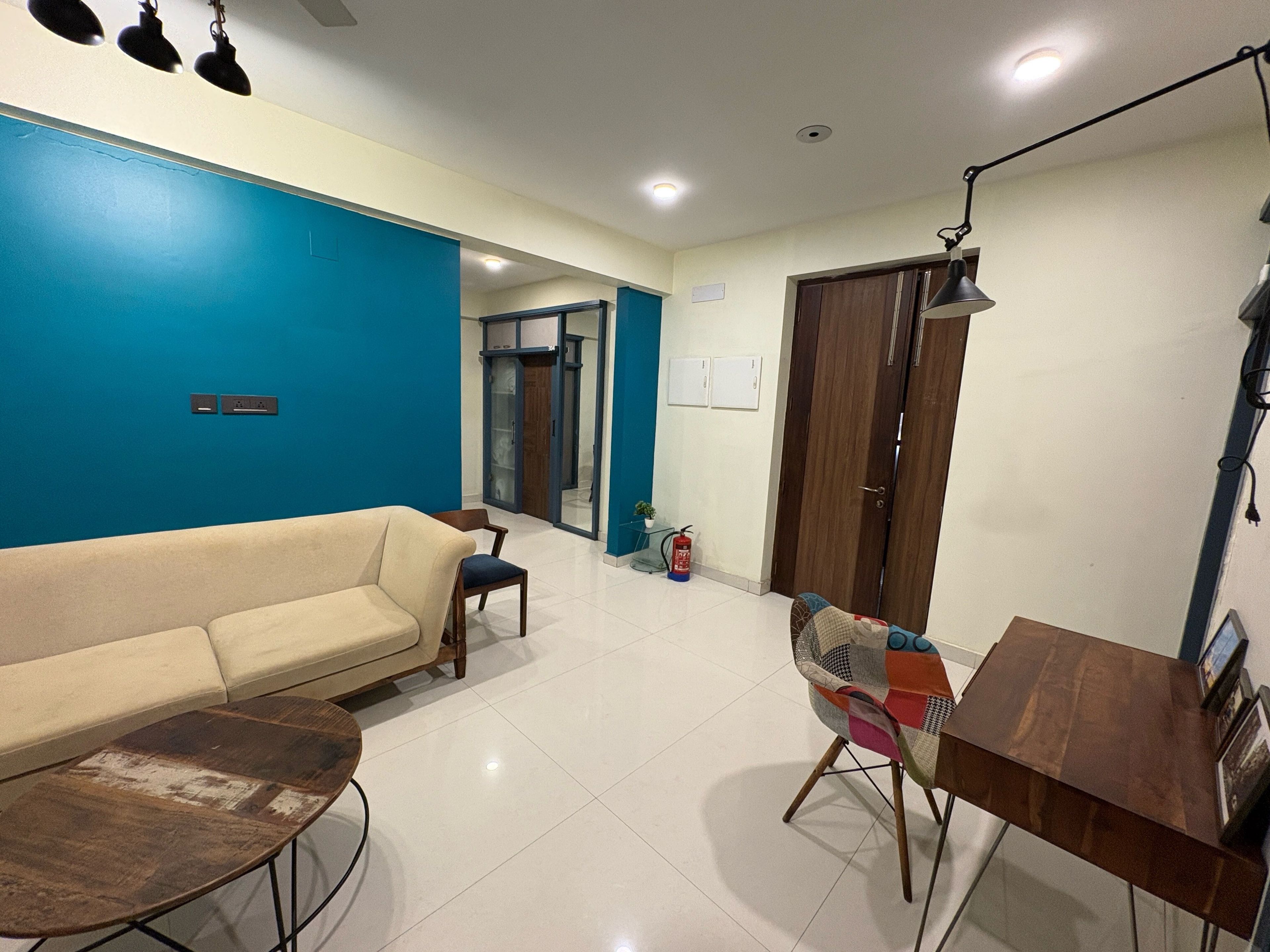 A living room with a sofa, a coffee table, a wooden side table, a lamp, and a door leading to another room.