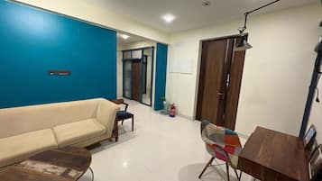 A living room with a sofa, a coffee table, a wooden side table, a lamp, and a door leading to another room.